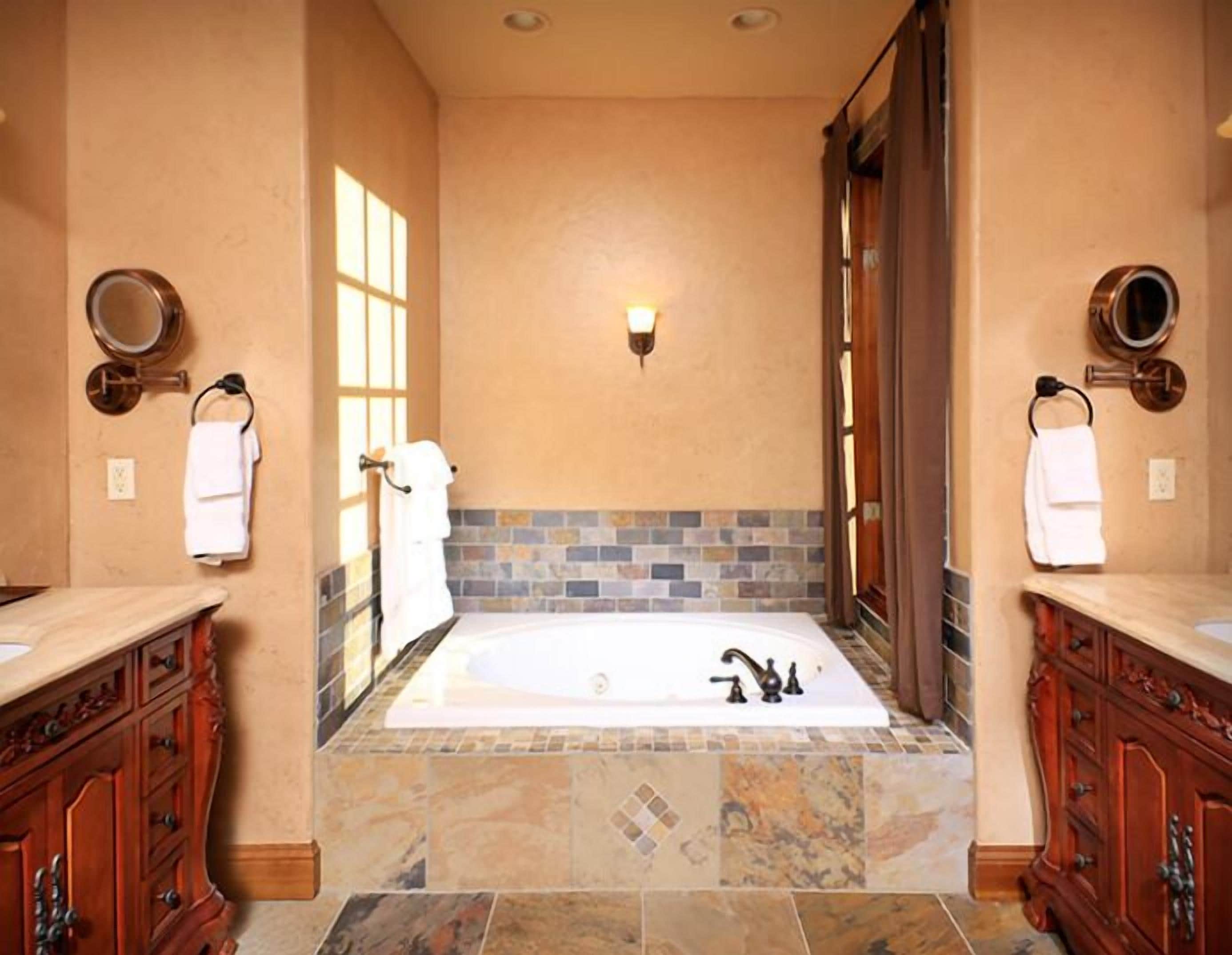 A bathroom with a large bathtub, two wooden cabinets, a tiled floor, and a wall-mounted light fixture.