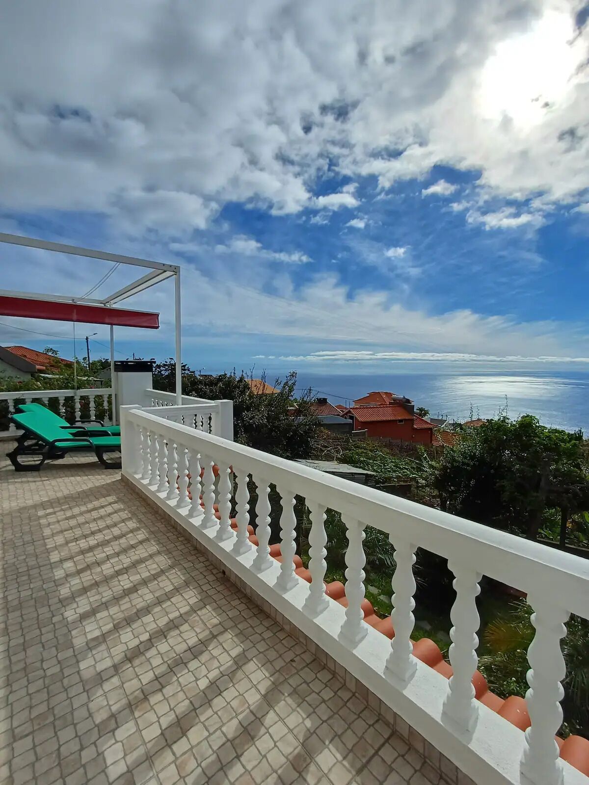 A balcony with a white balustrade, green lounge chairs, and a view of the sea and buildings in the distance.