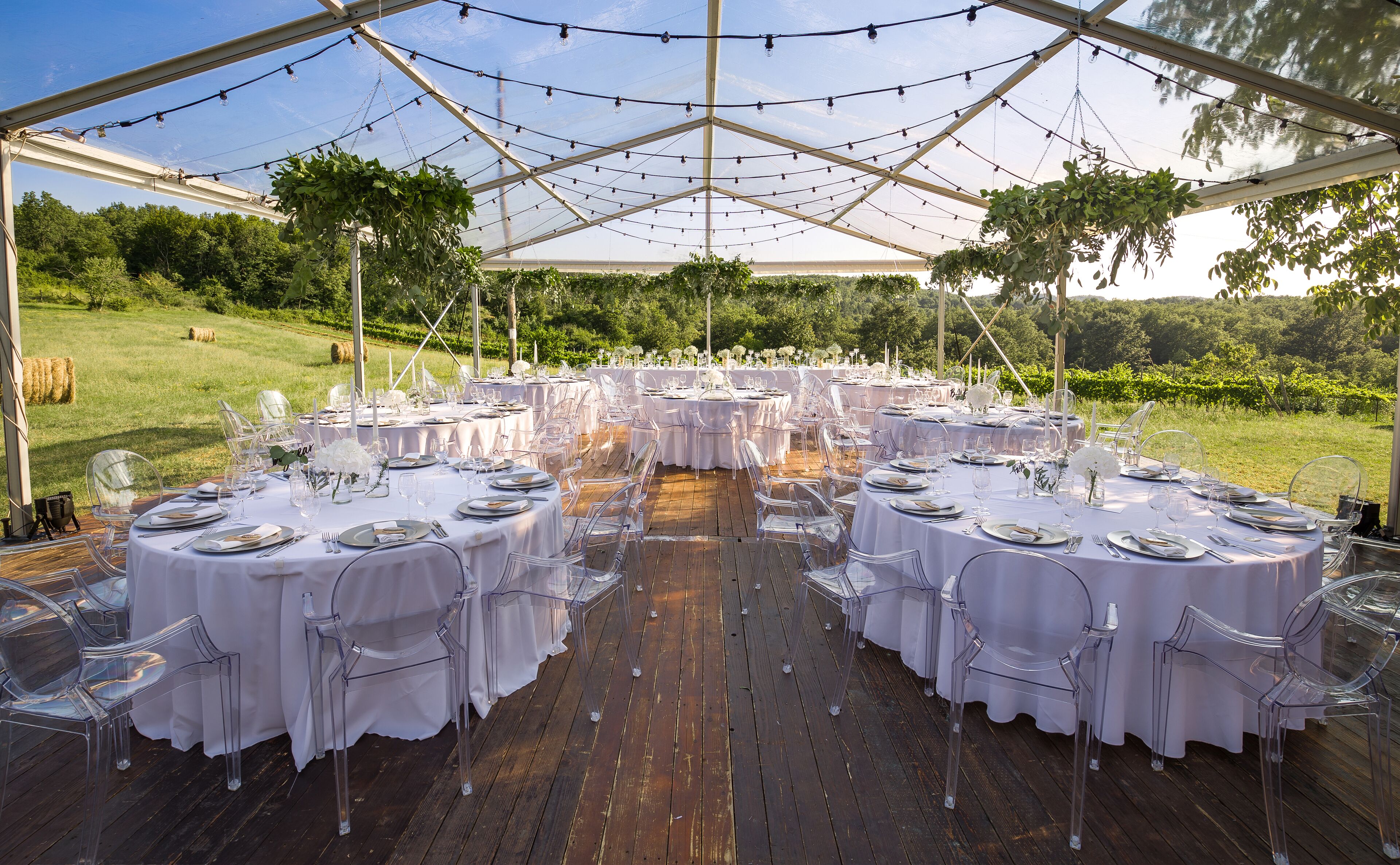 Un espace de restauration en plein air, aménagé sous une tente, avec des tables rondes dressées pour un événement formel, entouré d’une terrasse en bois et d’un vignoble en arrière-plan.