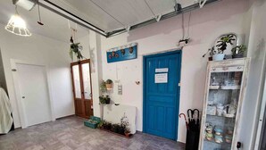 Un pasillo con una puerta azul, plantas en macetas, una vitrina de vidrio y piso de baldosas.