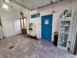 A hallway with a blue door, potted plants, a glass display case, and a tiled floor. - CASA PITA.  (San Justo de la Vega)