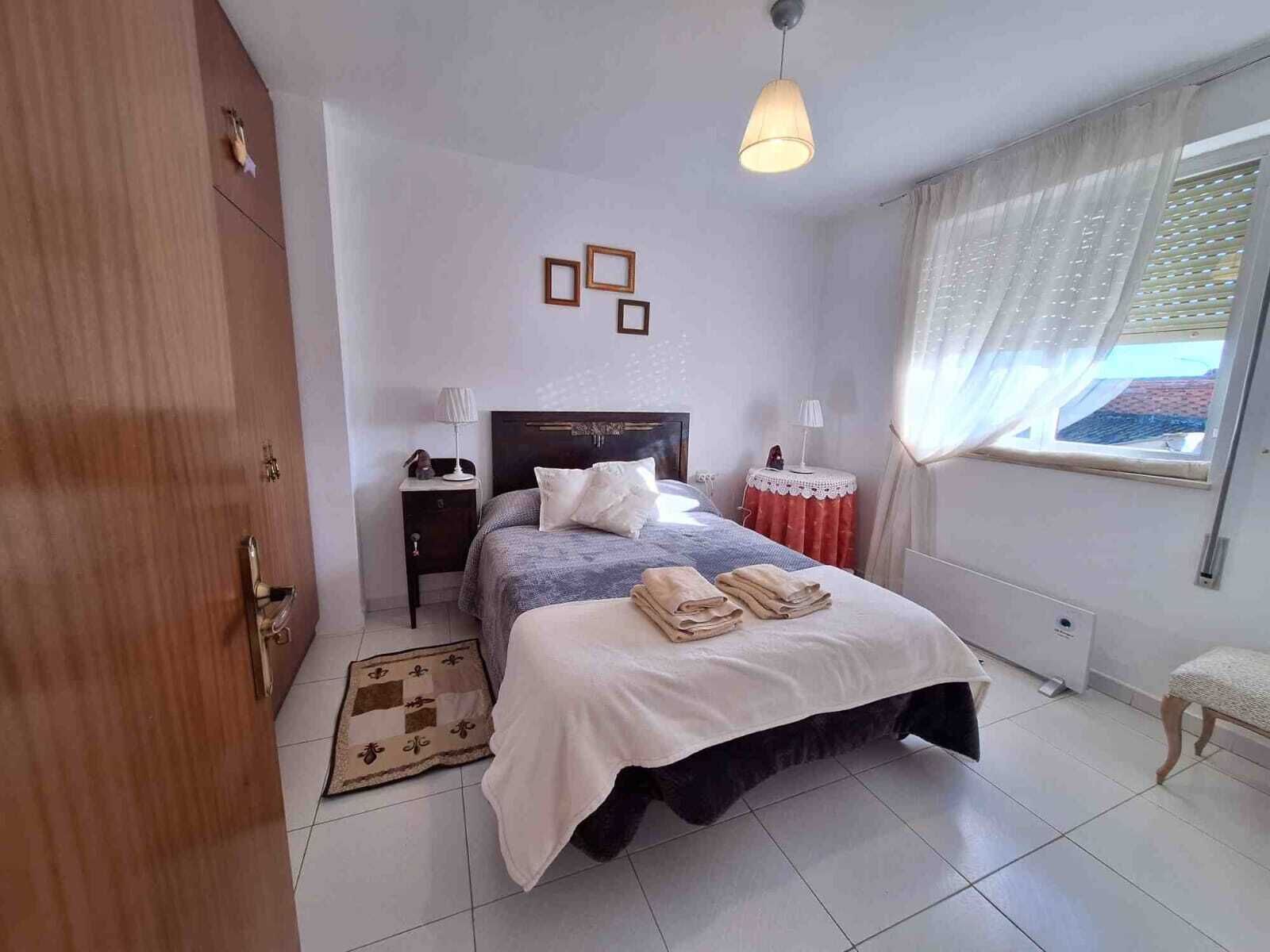 Een slaapkamer met een bed, nachtkastjes, een raam met gordijnen, een hanglamp en een deur.