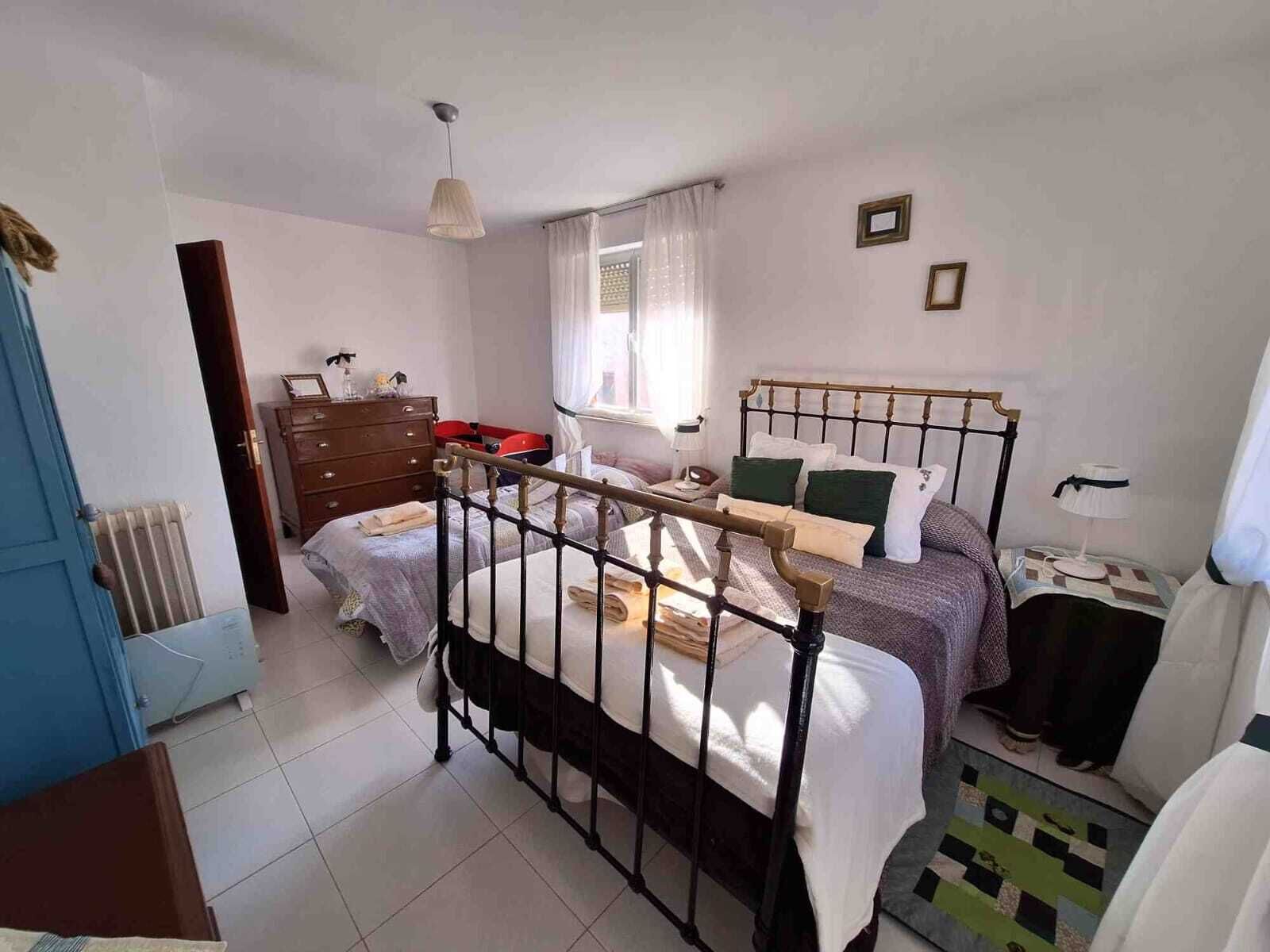 Un dormitorio con cama, cómoda, radiador y ventana con cortinas.