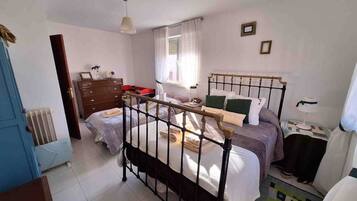 Un dormitorio con cama, cómoda, radiador y ventana con cortinas.