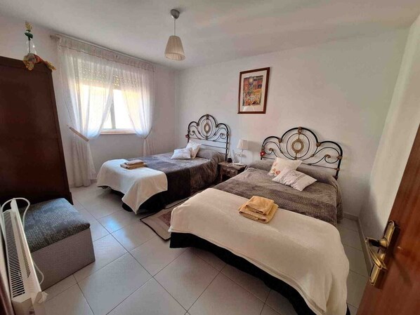 A bedroom with two beds, a window with curtains, a bedside table with a lamp, and a painting on the wall. - CASA PITA.  (San Justo de la Vega)