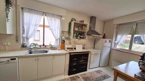 Una cocina compacta con pileta, estufa y heladera. Hay placares, una ventana con cortinas y piso de baldosas.