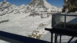 Ett snötäckt berg med en topp, en klippavsats och en metallkonstruktion med ett rutmönster.