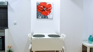 Une table à manger blanche, accompagnée de deux chaises, d’une petite plante en pot et d’une bouteille de couleur turquoise posée sur la table.