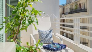 A balcony with a white chair, a patterned cushion, and a blue blanket.