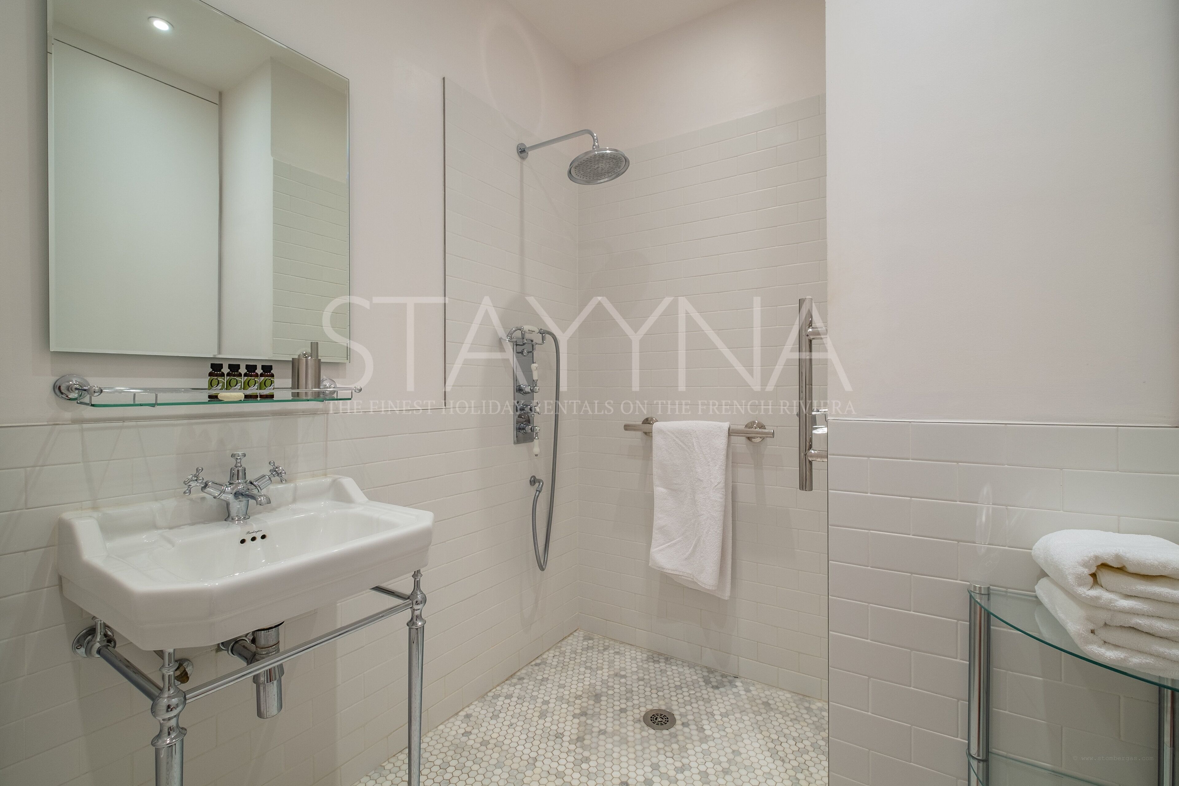 A modern bathroom with a white sink, a glass shower enclosure, and a glass-topped vanity.