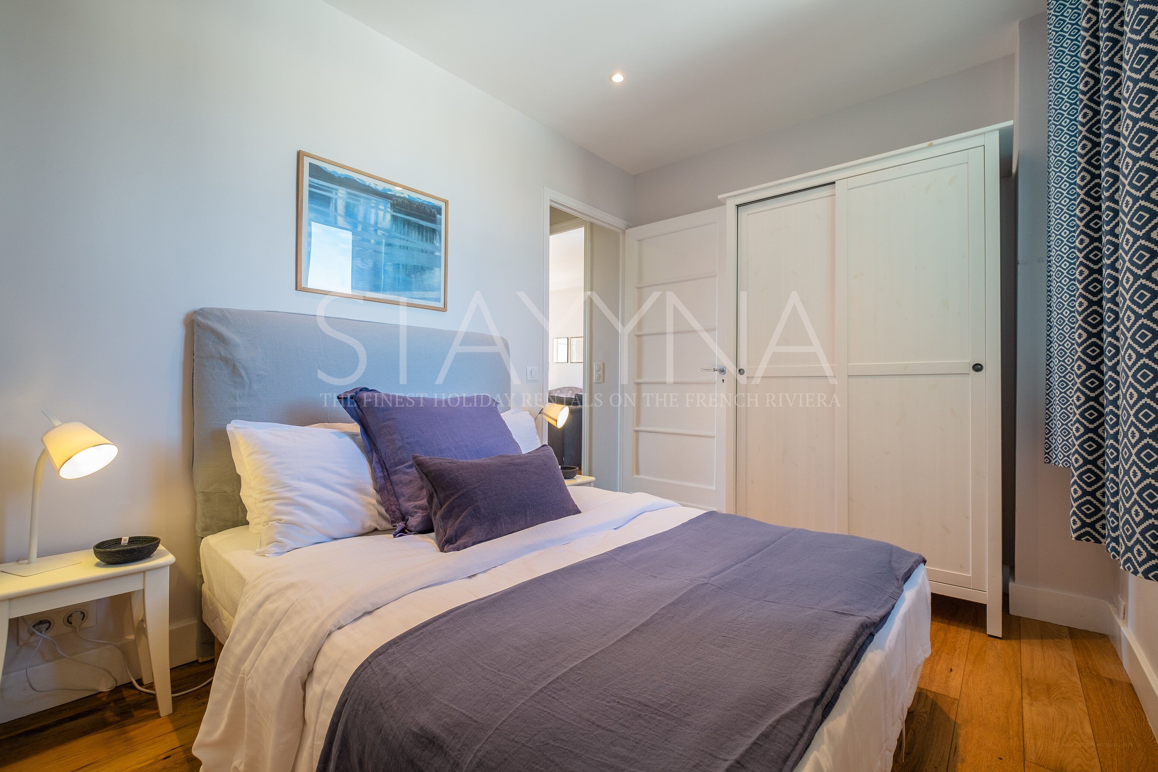 Een slaapkamer met een bed, nachtlampjes, een ingelijst schilderij aan de muur en een kledingkast.