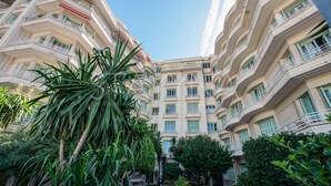 A multi-story residential building with balconies, a courtyard with greenery, and a clear sky.