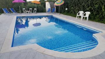 Ein Schwimmbecken mit Fliesenrand, umgeben von Liegestühlen und Sonnenschirmen.