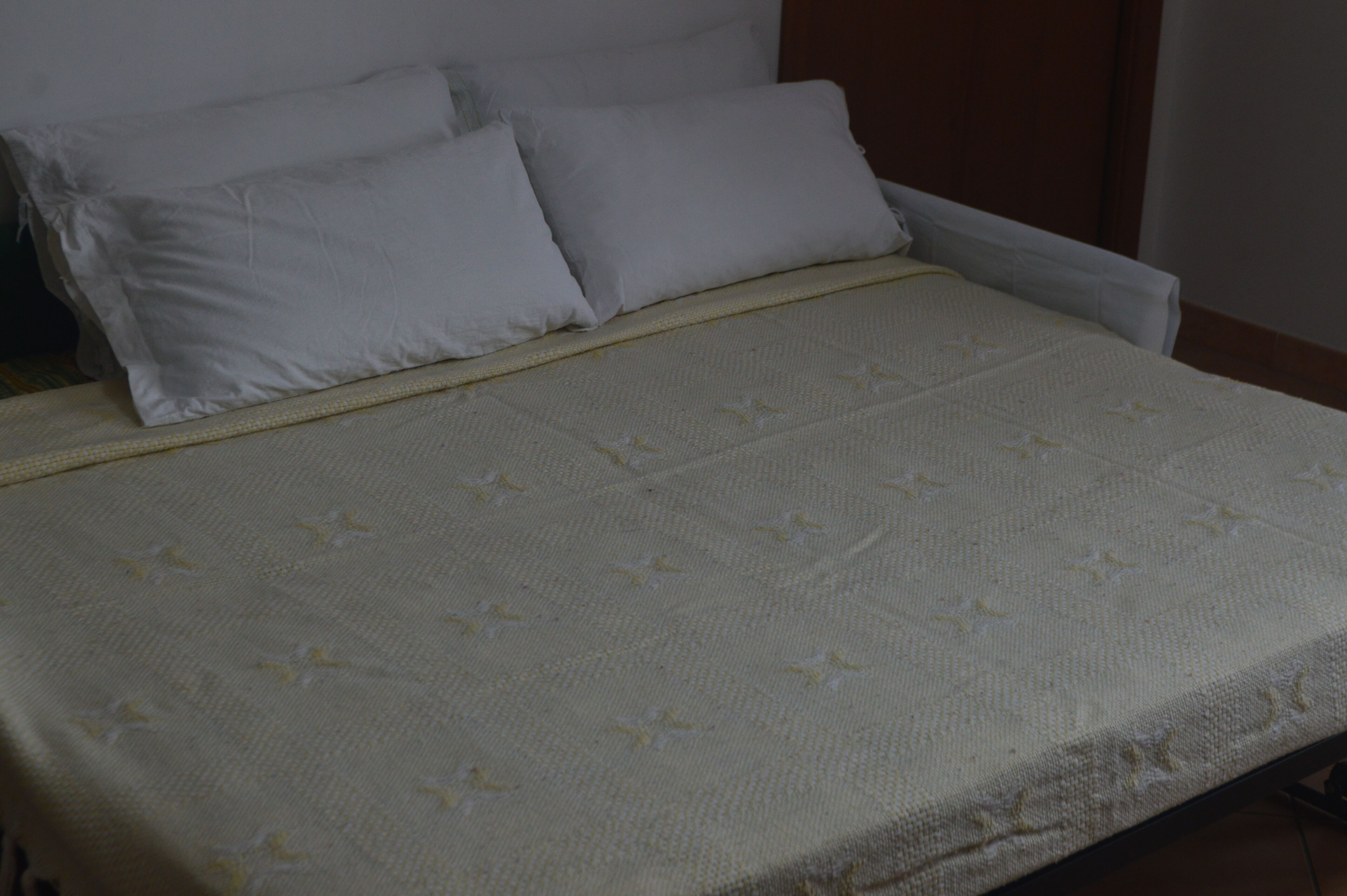 A bed with a white mattress and a white blanket with a subtle pattern.