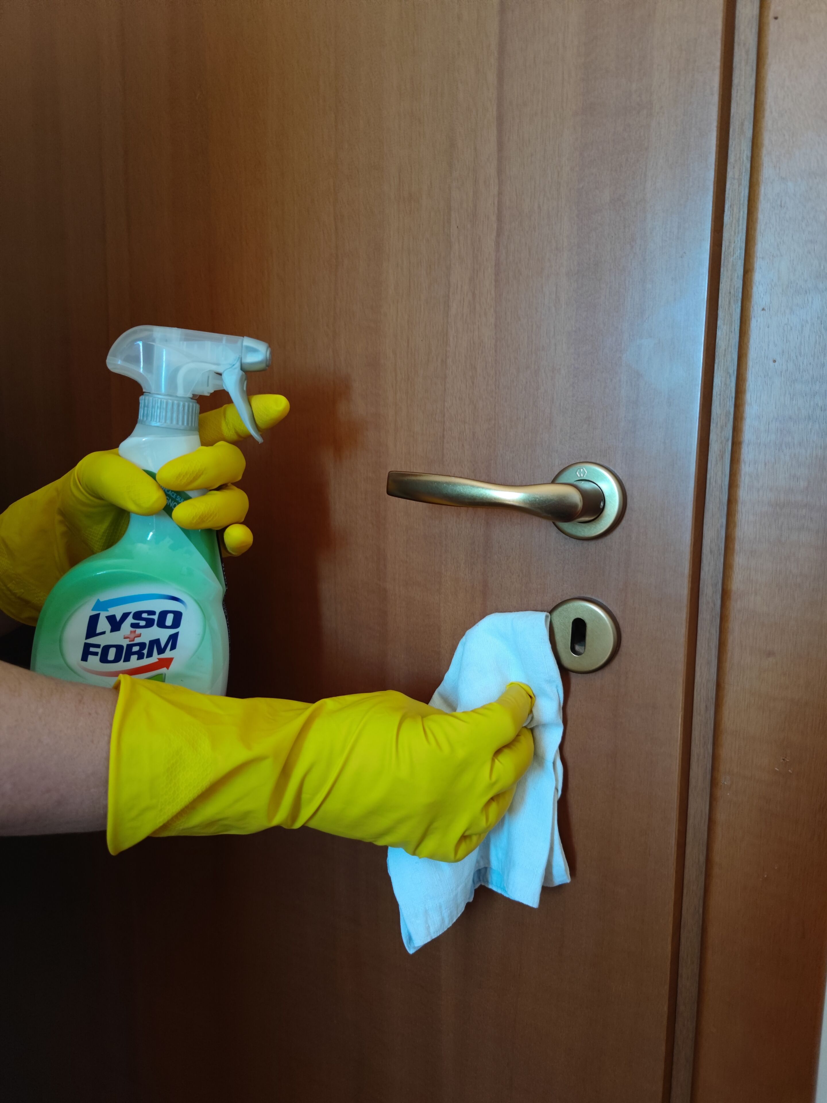 A person cleaning a door handle with a cloth and a Lysso Form spray bottle.