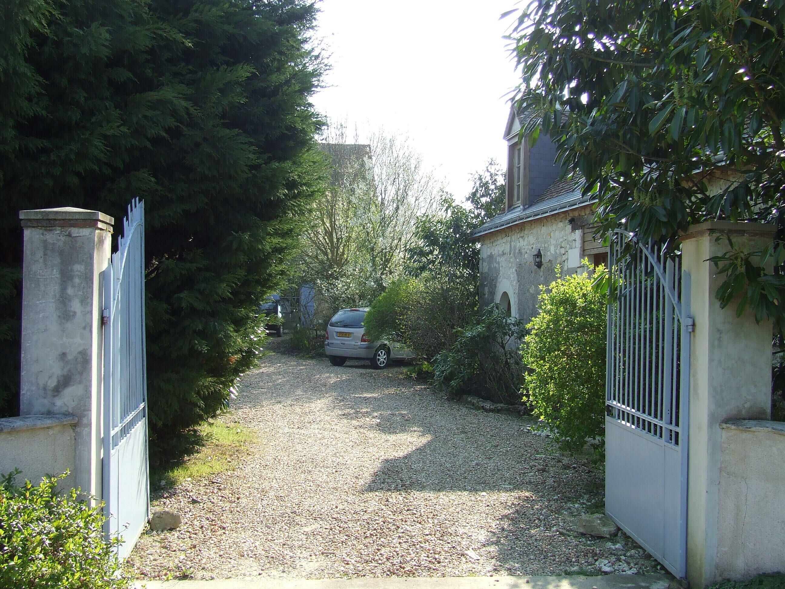 A gravel driveway leading to a gated entrance with a parked car.