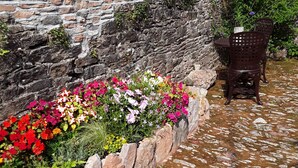 Un muro de piedra con un cantero de flores y un banco.
