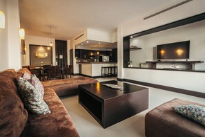 Een moderne woonkamer met een grote bruine bank, een zwarte salontafel en een aan de muur bevestigde televisie.