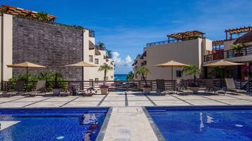 A pool area with two pools, lounge chairs, umbrellas, and a view of the ocean.