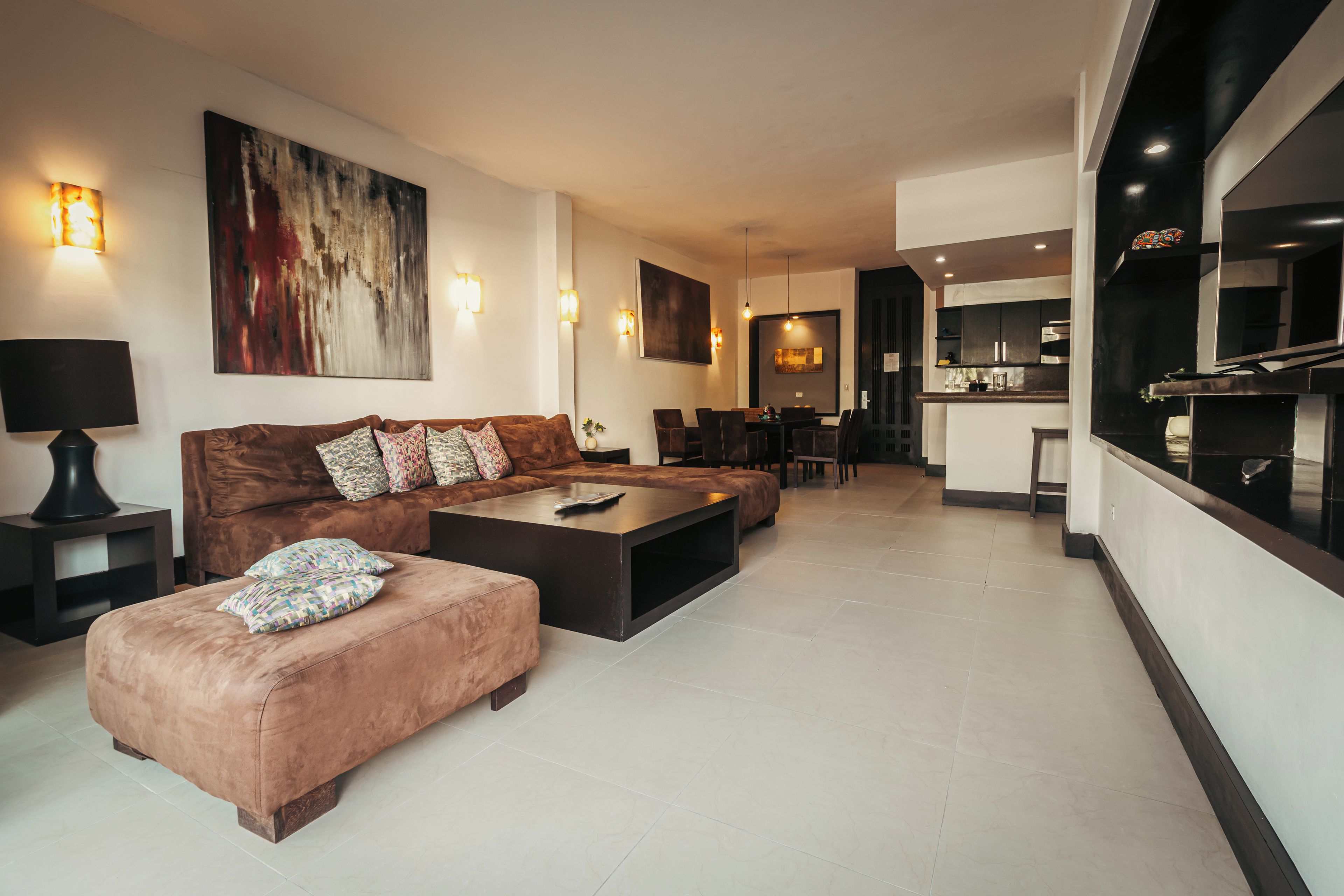 A modern living room with a sofa, ottoman, and coffee table, a dining area with chairs, and a kitchen with a large island.