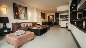 A modern living room with a sofa, ottoman, and coffee table, a dining area with chairs, and a kitchen with a large island.
