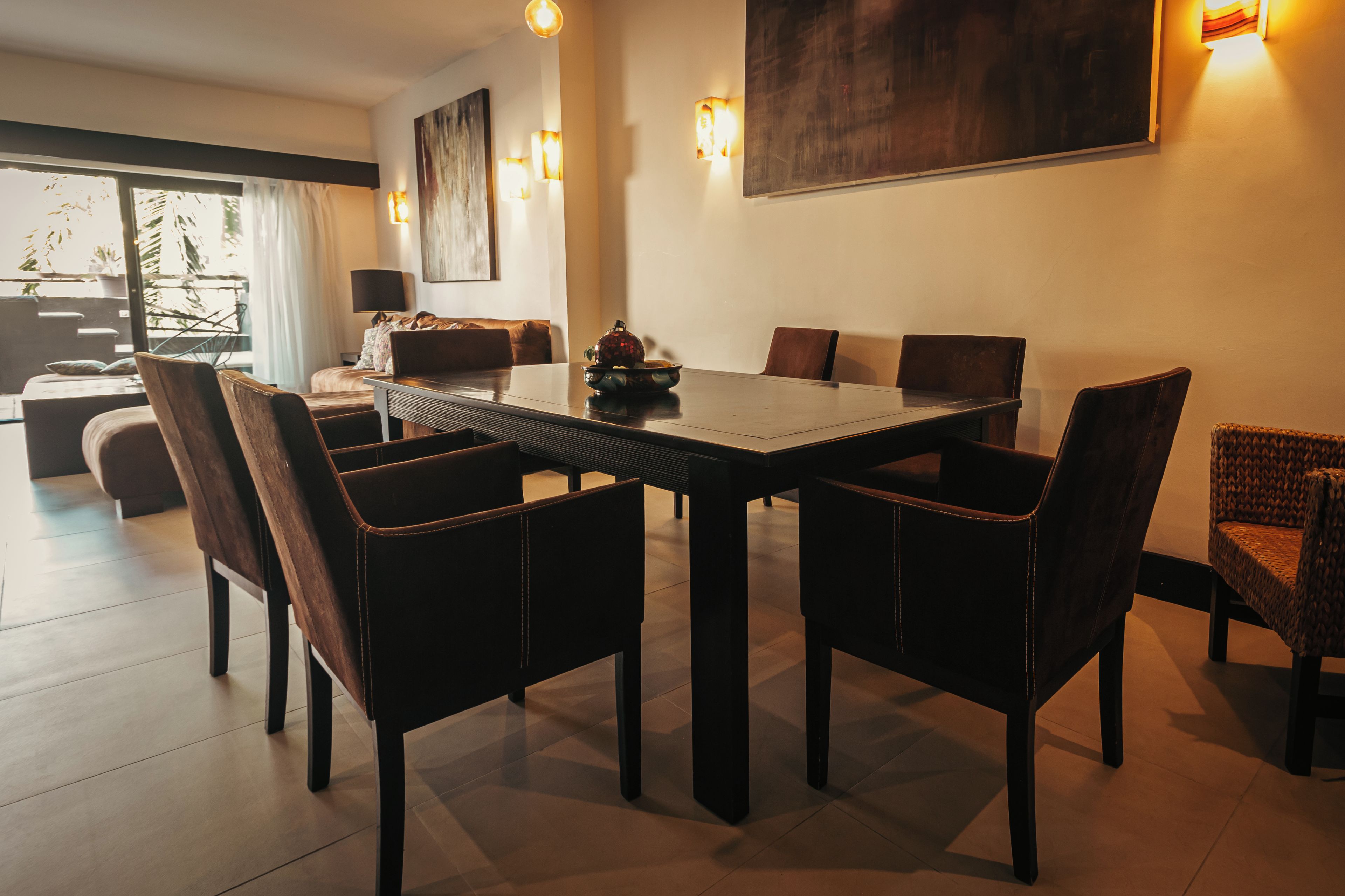 A modern dining area with a rectangular table surrounded by six chairs, a sofa, and a dining table with a decorative bowl.