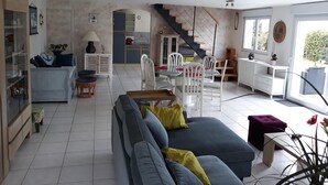 Un vaste espace de vie comprenant un canapé, une table à manger et des chaises. Un escalier mène à l’étage supérieur.