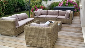 Une terrasse dotée de meubles en osier, notamment d’un canapé et de deux fauteuils, ainsi que d’une table basse.