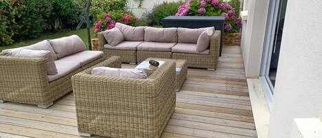 Un patio con mobiliario de mimbre, incluyendo un sofá y dos sillones, además de una mesa de centro.