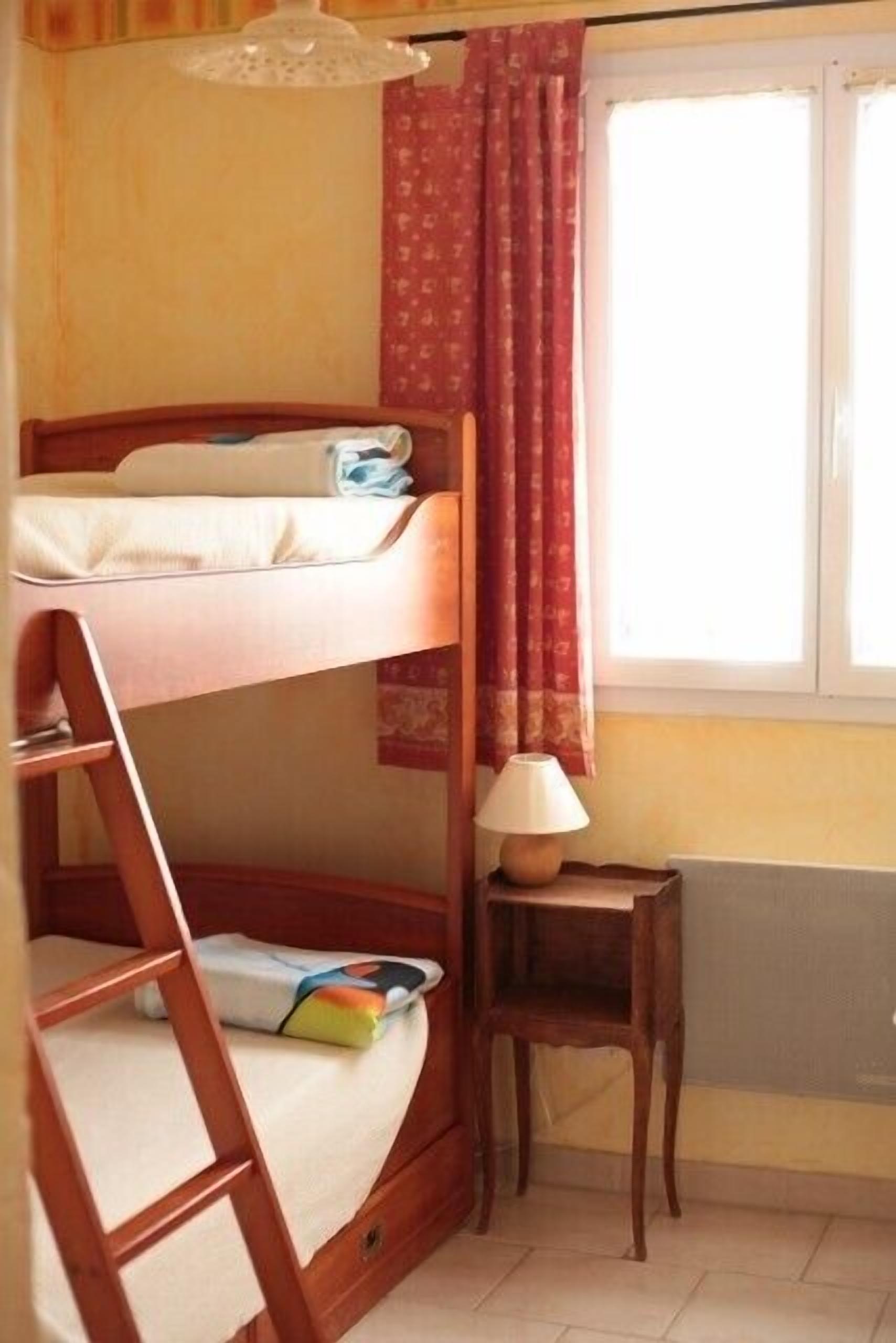 A bunk bed room with a window, a lamp, and a radiator.