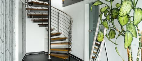 Un interior moderno con una escalera en espiral, suelo oscuro y una gran planta en maceta.