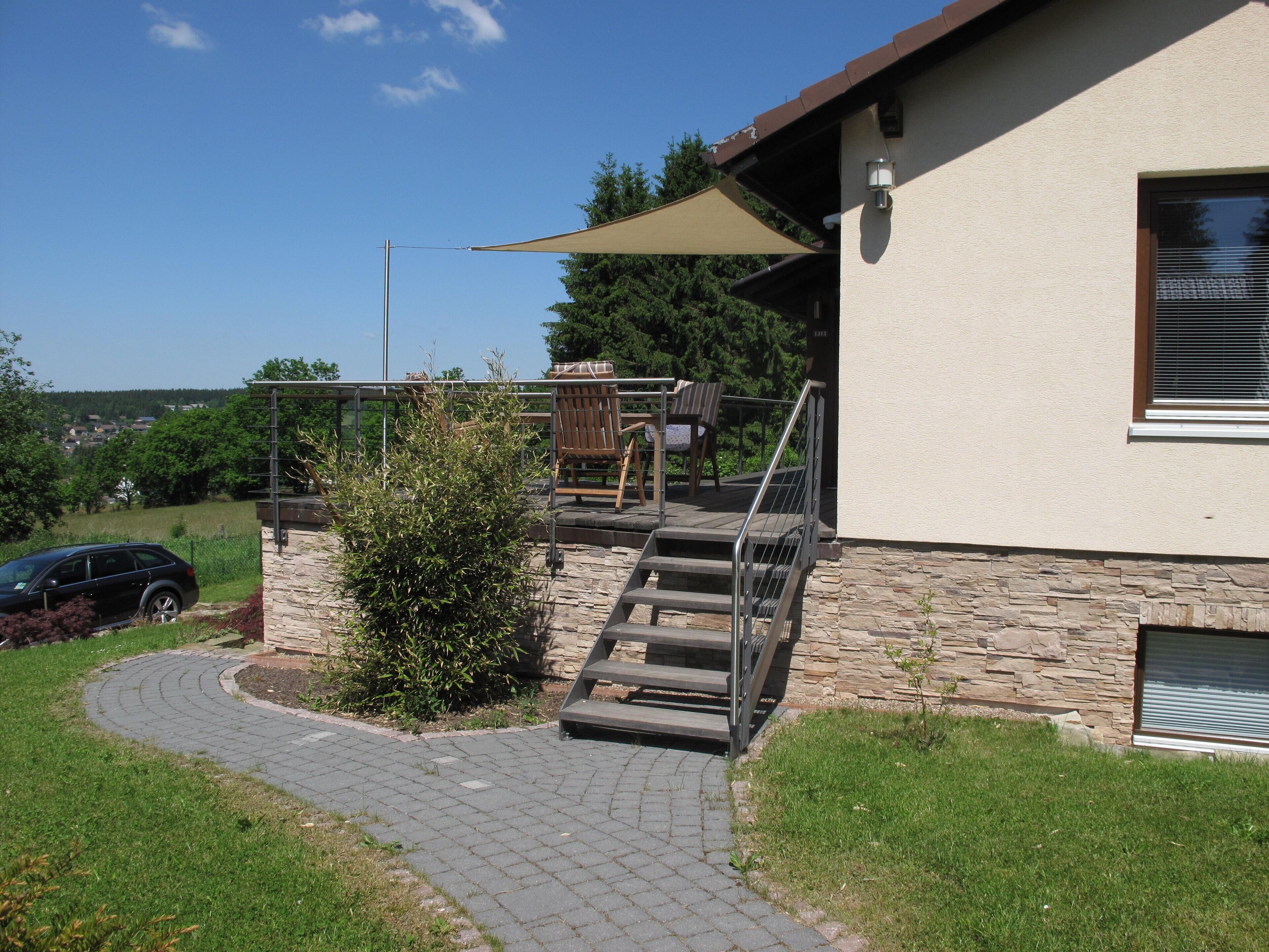 A house with a stone facade, a wooden deck with outdoor furniture, and a car parked nearby.