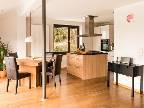 A modern kitchen with wooden cabinets, a central island, and a dining area with a table and chairs. - Detached vacation home - luxury & nature with a view (sauna, fireplace, lounge couch) (Silberborn)