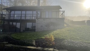 Una casa moderna amb façana de pedra, grans finestres i un balcó.