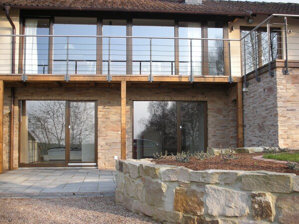 A modern two-story house with large glass doors and windows, stone walls, and a balcony. - Detached vacation home - luxury & nature with a view (sauna, fireplace, lounge couch) (Silberborn)