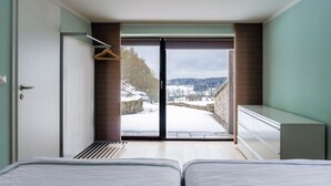 Habitació d'hotel moderna amb dos llits, una gran porta corredissa de vidre que dona a una zona exterior nevada i vista al camp de paisatge.
