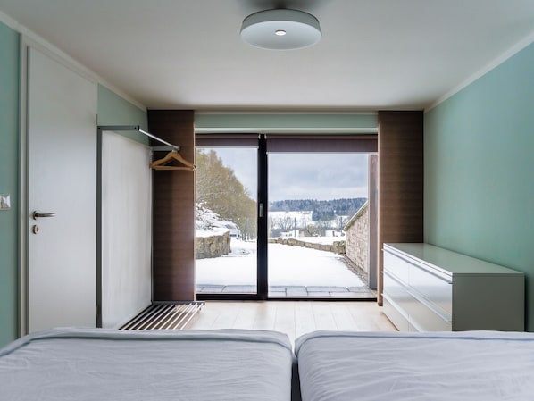 Ein modernes Hotelzimmer mit zwei Betten, einer großen Schiebeglastür, die zu einer verschneiten Außenanlage führt, und Blick auf die Landschaft.