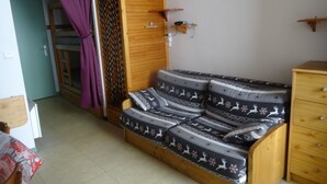 Ein kleines, gemütliches Zimmer mit einer Holz-Couch, einem Holzschrank und einem kleinen Tisch.