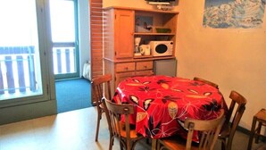 Ein Essbereich mit Tisch, der mit einer roten Tischdecke bedeckt ist, Holzsesseln, einem Fernseher auf einem Regal und einem Gemälde an der Wand.