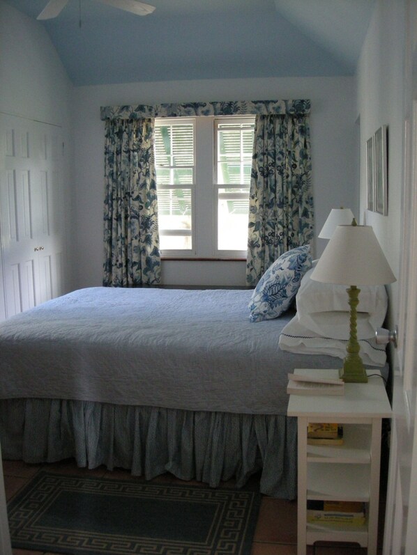Une chambre à coucher avec un lit, une table de chevet, une lampe, une fenêtre avec des rideaux et une porte.