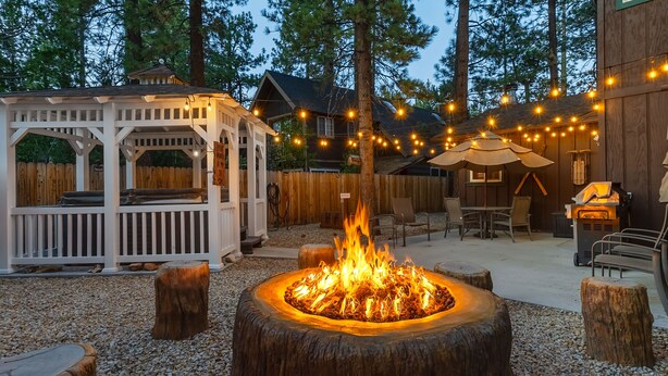 A backyard with a fire pit, wooden deck, outdoor furniture, and string lights. - Family cabin: Hot tub, firepit, game room, fenced, BBQ, movie lineup (Big Bear)