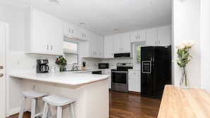 A modern kitchen with white cabinetry, a central island with stools, a black refrigerator, and a wooden countertop. - Oak Knob Equestrian Home (Campobello)