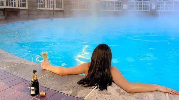 Une femme se détend au bord d’une piscine, une bouteille de champagne et un verre à proximité.