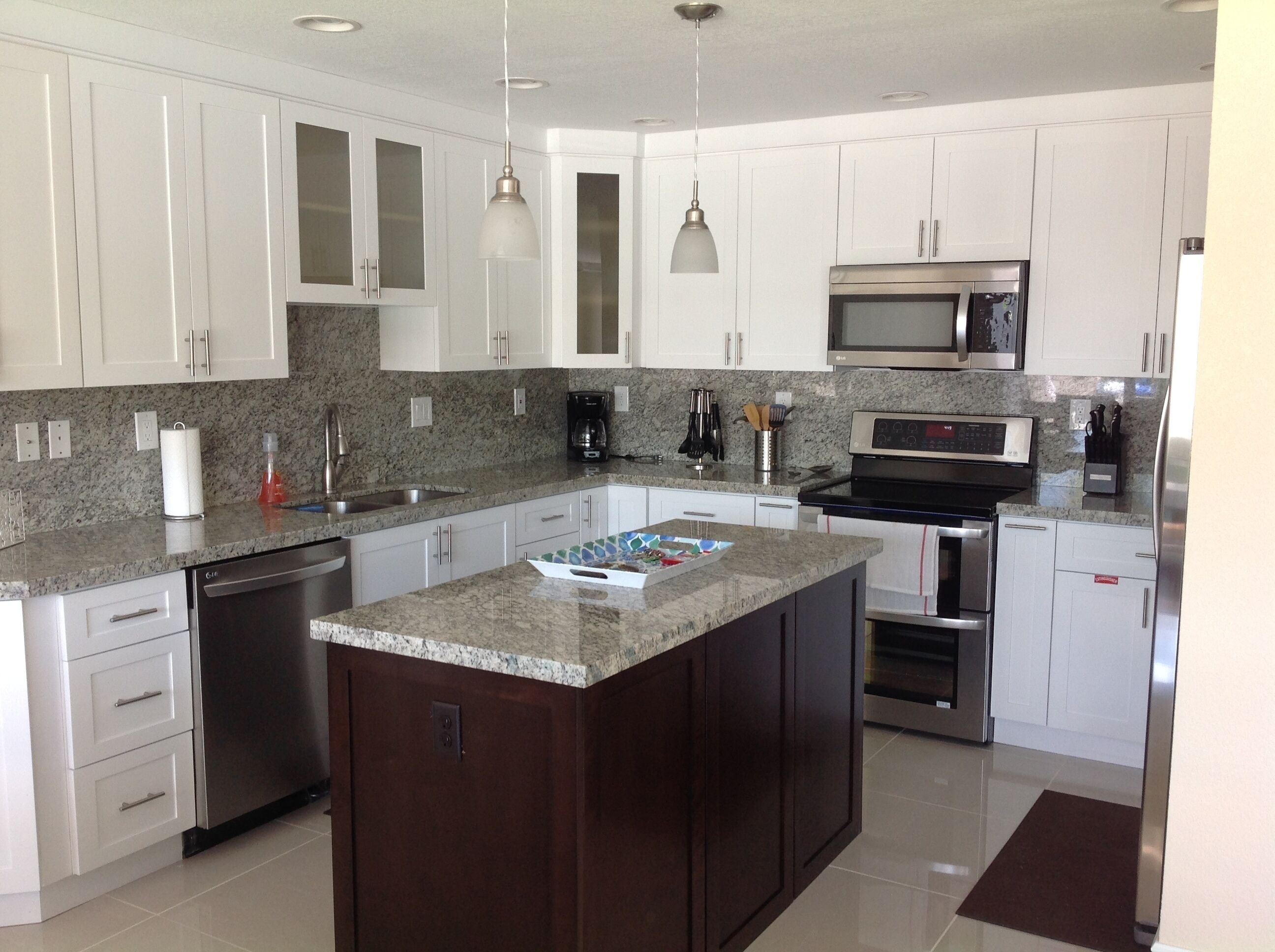 A modern kitchen with white cabinets, granite countertops, stainless steel appliances, and pendant lighting.