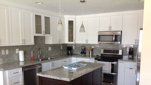 A modern kitchen with white cabinets, granite countertops, stainless steel appliances, and pendant lighting. - Compelling Canal Home with Pool & Large Dock on each side-Cabana Club Included (Key Colony Beach)