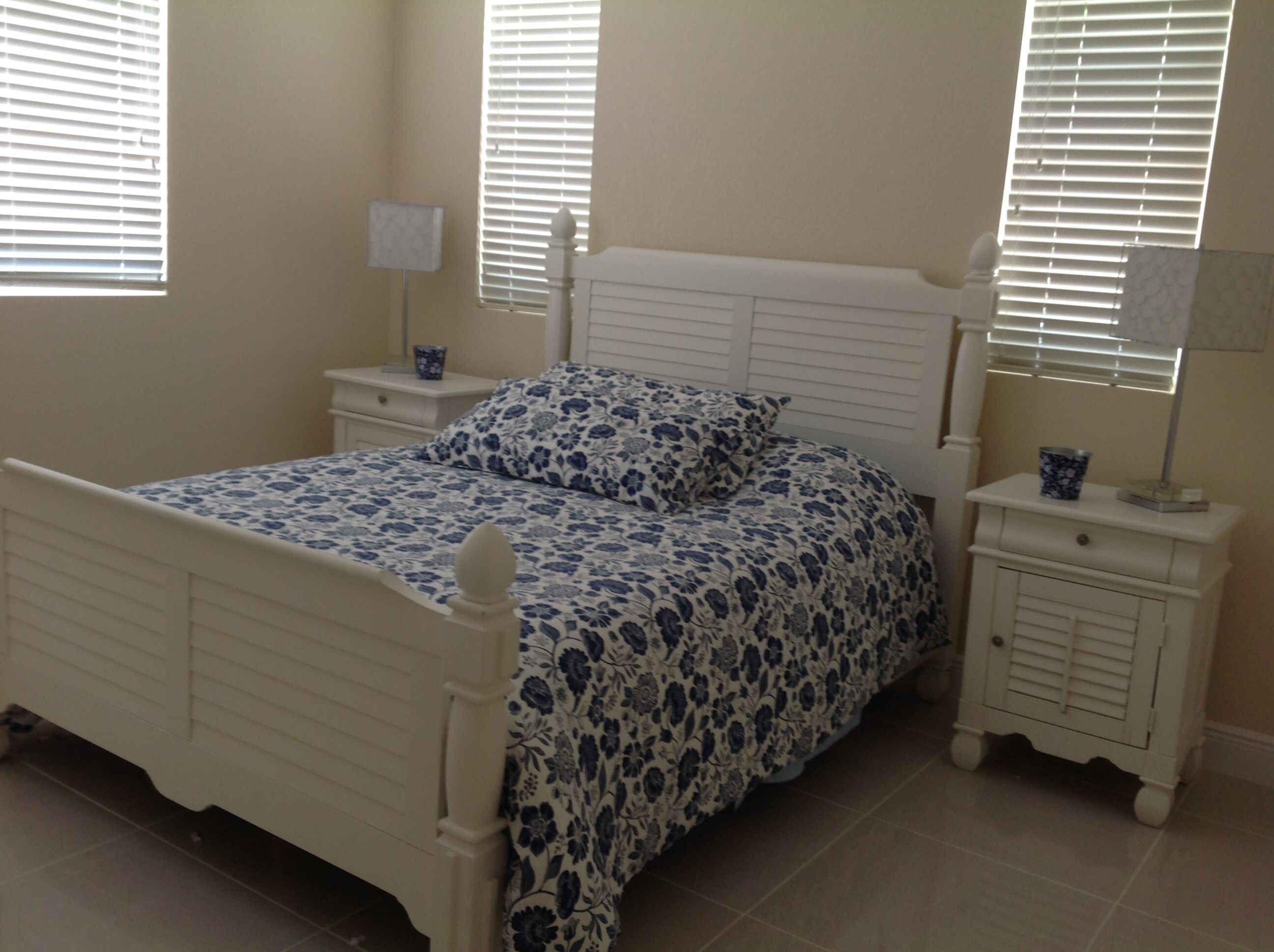 Une chambre avec un lit blanc, des tables de chevet assorties et une fenêtre avec des stores.