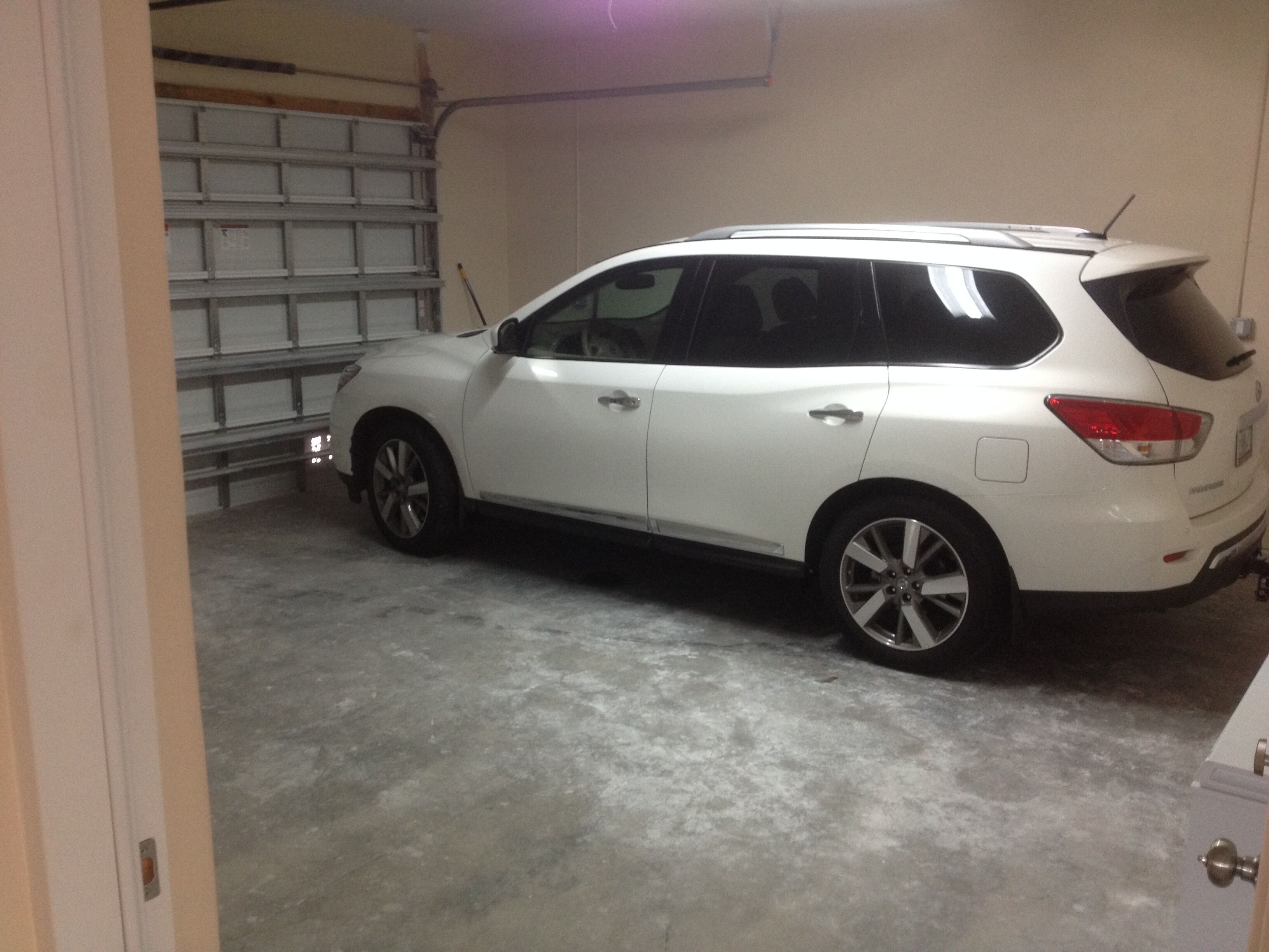 A white SUV parked in a garage with a concrete floor and a metal garage door in the background.