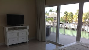 A hotel room with a balcony, a flat-screen TV on a white dresser, and a floral bedspread. - Compelling Canal Home with Pool & Large Dock on each side-Cabana Club Included (Key Colony Beach)