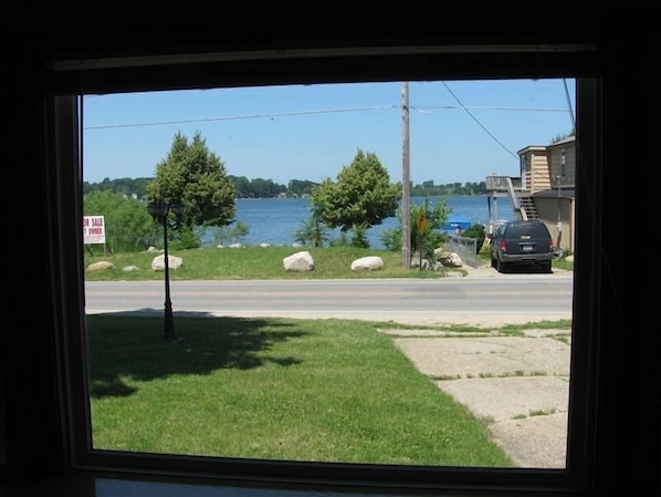 A view of a road with a 'For Sale' sign, a grassy area, a body of water, and a building with a car parked in front.