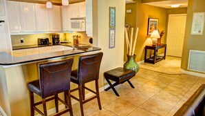 A kitchen with white cabinets, a black countertop, and two bar stools. There is a vase with bamboo sticks and a small table with a lamp. - Fabulous condo, excellent reviews!! 2 chairs and 1 umbrella (Available Mar-Oct) (Navarre)